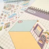 Carnet à spirales contenant 20 scènes de stickers isométrique 3D à composer soi-même sur le thème des boutiques kawaii et mignonnes. Activité créative pour adulte pour gérer le stress.