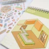 Carnet à spirales contenant 20 scènes de stickers isométrique 3D à composer soi-même sur le thème des boutiques kawaii et mignonnes. Activité créative pour adulte pour gérer le stress.